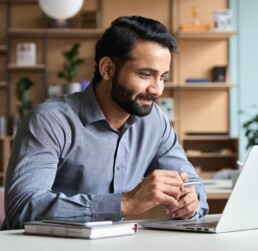 Smiling bearded indian businessman working on laptop at home office